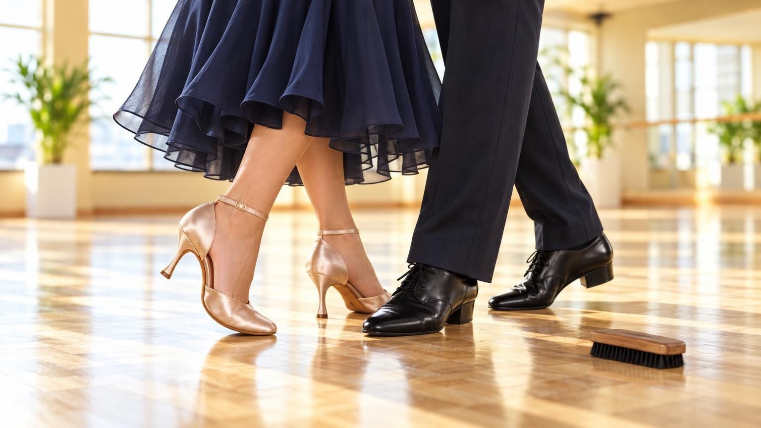 Close-up of a lady's closed-toe satin court shoe with an ankle strap and a man's black lace-up dance Oxford standing side by side on a light parquet floor, a small suede-